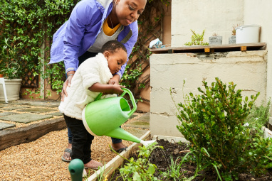 Woman helping young child to water plants in garden