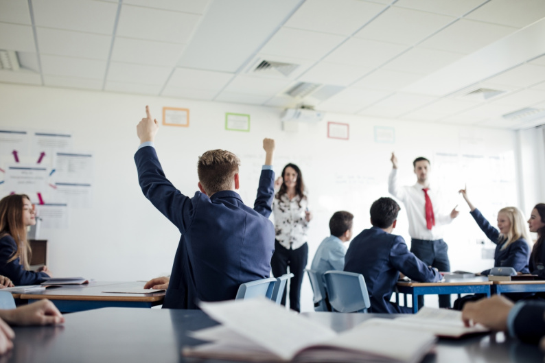 Young people in classroom with raised hands