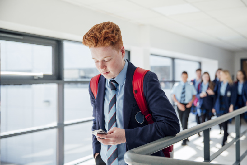 Young person walking on his own in a corridor looking at phone