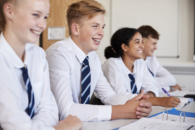 Four secondary school age pupils smiling at their desk