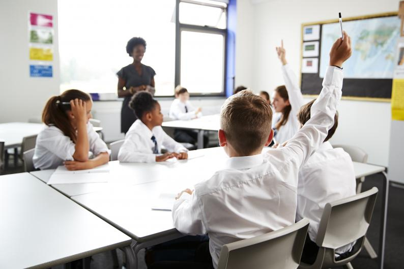 Children in a classroom, with one child with a raised hand